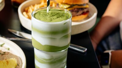 A bright green drink with a burger and chips behind it