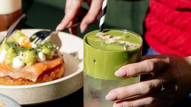 A hand holding a green iced drink and a savoury food dish nearby