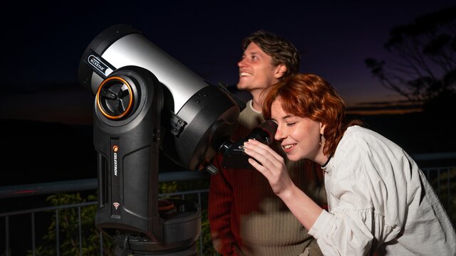 A couple look through a telescope at night time