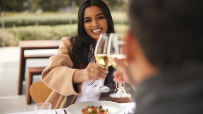 A woman dines with someone and is smiling holding a glass of white wine