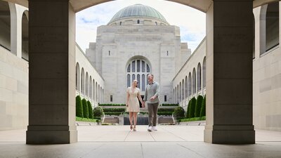 A couple holding hands and walk through an open wide section of the Australian War Memorial