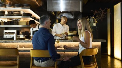 Two people dining together with sushi chefs working in the background