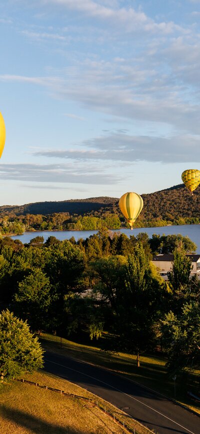 A bright yellow hot air balloon in focus with some colourful balloons drifting in the sky behind it