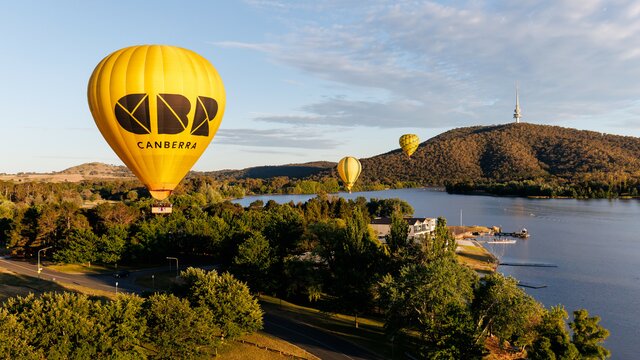 A bright yellow hot air balloon in focus with some colourful balloons drifting in the sky behind it