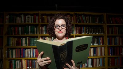 Woman reading book in front of bookshelf