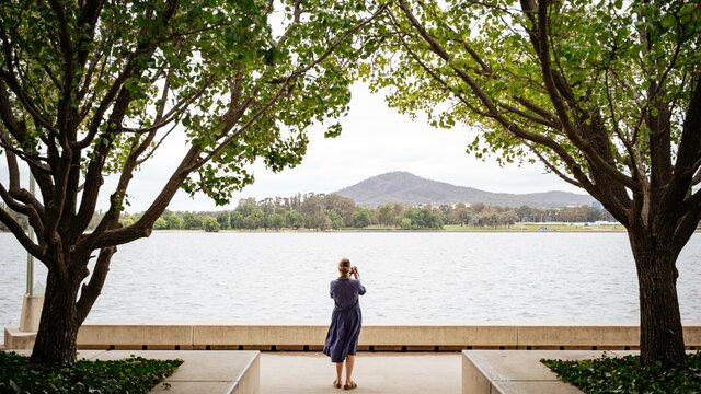 The back of a woman photographing Lake Burley Griffin