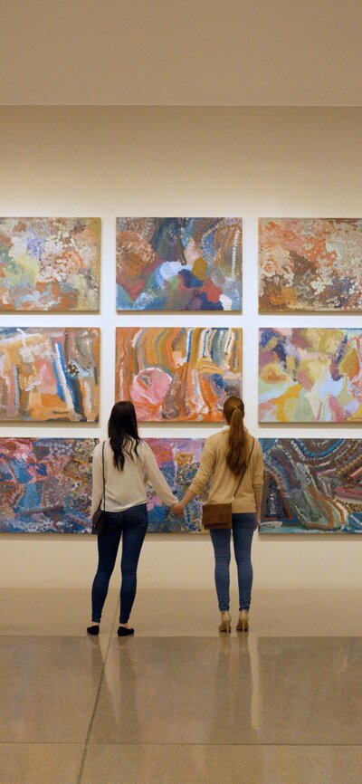 Female couple holding hands in front of Indigenous artwork at the National Gallery of Australia | © CRUX
