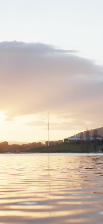Sunset view of Lake Burley Griffin and a GoBoat full of humans enjoying the view of Black Mountain Tower in the background.