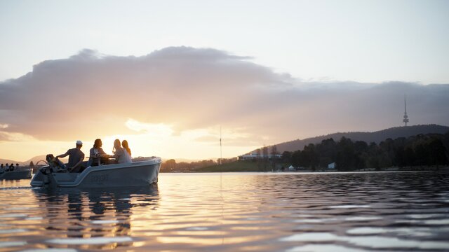 Sunset view of Lake Burley Griffin and a GoBoat full of humans enjoying the view of Black Mountain Tower in the background.