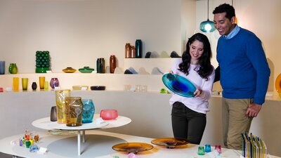 A couple looking at a blue vase at a shop full of glassworks.