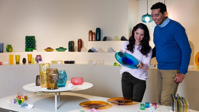 A couple looking at a blue vase at a shop full of glassworks.