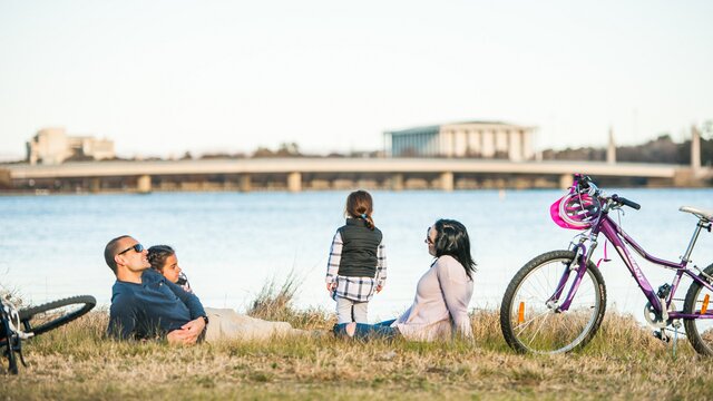 A couple with two young kids relaxing next to their bikes near the lake.