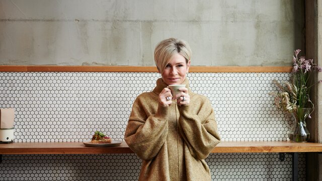 Emma Macdonald sips on a hot coffee while leaning back upon a wooden bench.