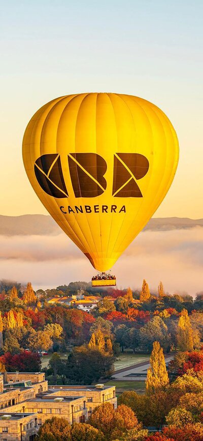 The iconic hot air balloon with 'CBR' written on it flying over Canberra during sunrise.