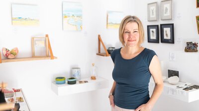 The owner of Gallery of Small Things Anne Masters standing infront of artworks.