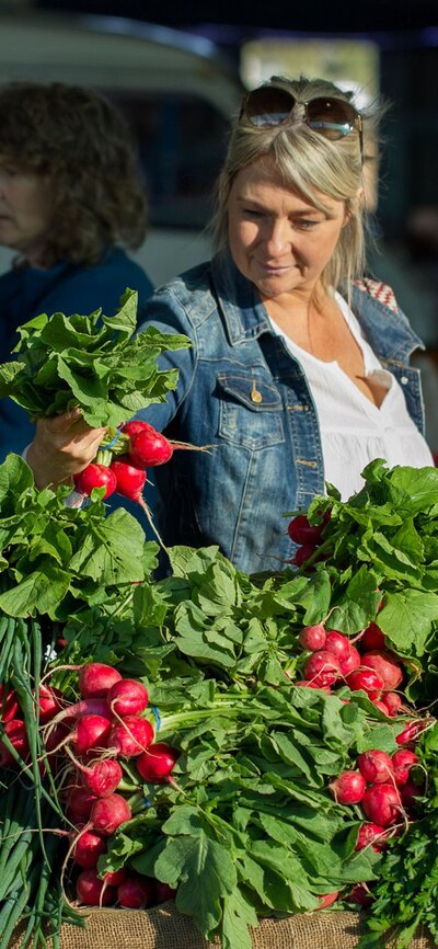 A woman in a demin jacket buying fresh radishes.
