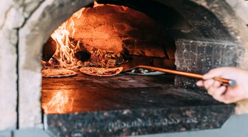 Pizza being put in a large woodfired oven