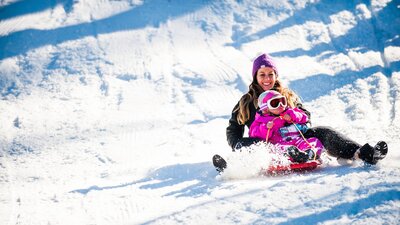 A child and her mother going down the snow at Corin Forest in a tobaggan.