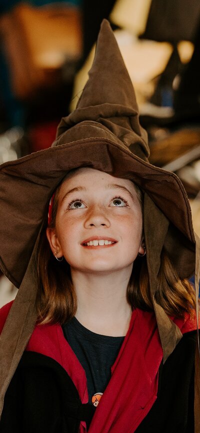 A young girl wearing a pointed witches' hat and harry potter robes.