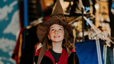 A young girl wearing a pointed witches' hat and harry potter robes.