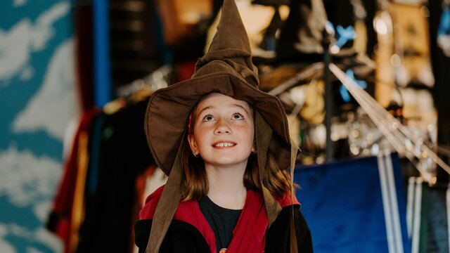 A young girl wearing a pointed witches' hat and harry potter robes.