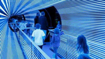 Visitors to Questacon walk across the light tunnel bridge.