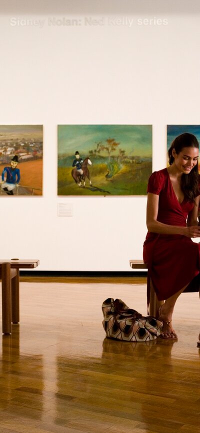 Two people sitting on a bench with art in the background.