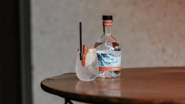A bottle of Big River Distillery Gin and a cocktail served on a table.