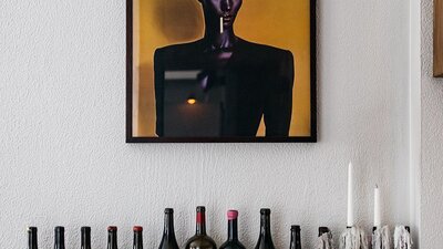 A line up of wine bottles sitting underneath a bold yellow painting.