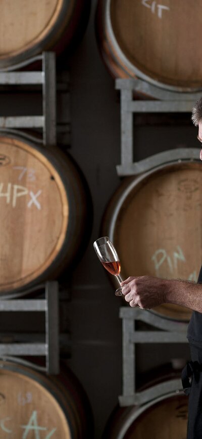 A man enjoying a glass of wine surrounded by wooden barrels of wine at Lerida Estate winery.