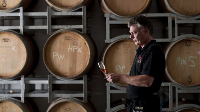 A man enjoying a glass of wine surrounded by wooden barrels of wine at Lerida Estate winery.