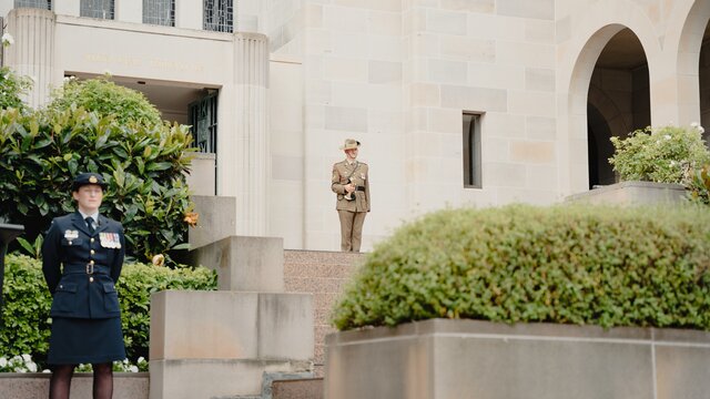 Soldiers and navy officer standing to attention on the steps at the Memorial.