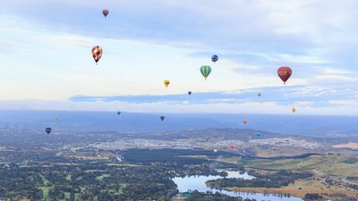 20 hot air balloons above the lake and hills of Canberra