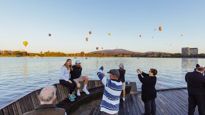 People taking photos in front of hot air balloons by the lake