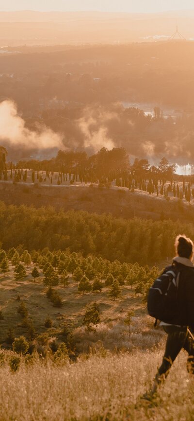 A woman walking across a hill overlooking Lake Burley Griffin and the National Arboretum.