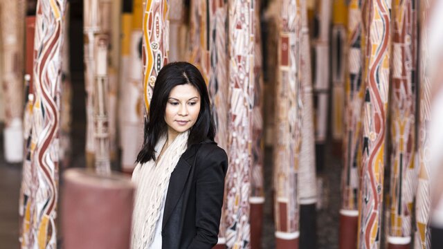 A woman in a black blazer walking between indigenous memorial poles.