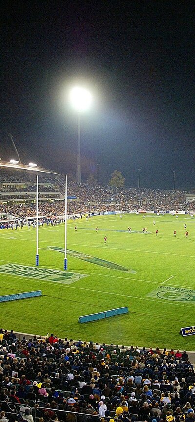 A large crowded stadium at night with a rugby game.