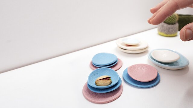 Hands move around small blue, pink, and white ceramic dishes at the Gallery of Small Things