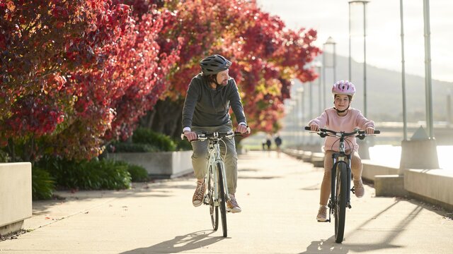 Father and daughter cycling near a lake with autumn trees in the background