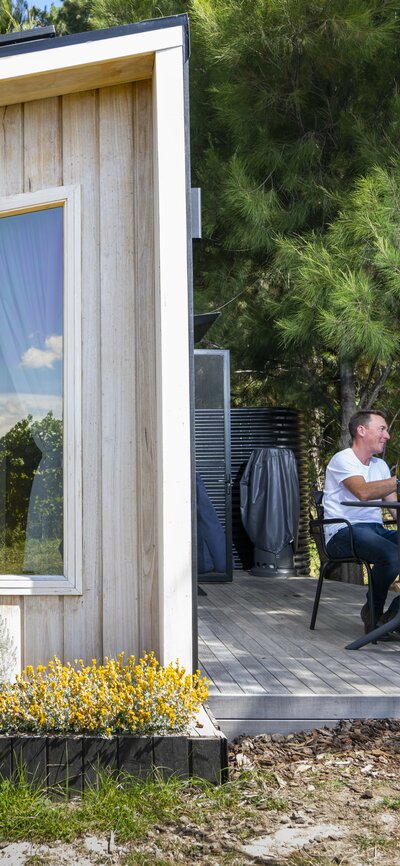 A couple sits outdoors beside a tiny house