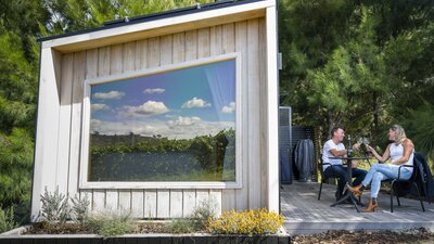 A couple sits outdoors beside a tiny house