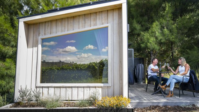 A couple sits outdoors beside a tiny house