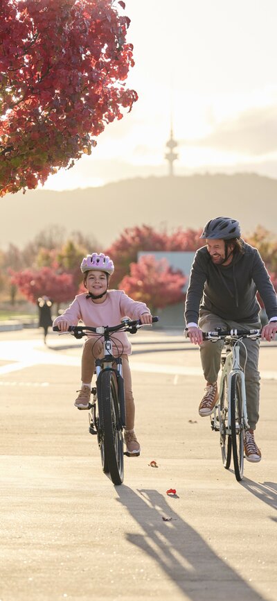 A father and daughter cycle by the lake amongst autumn leaves 