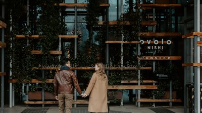A couple holds hand in front of an urban hotel