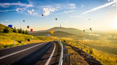 Long road with hot air balloons drifting in the background.