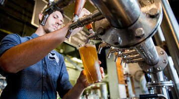 © Sean Davey Vision of beer being poured from underneath the taps, man with dark hair pours the light coloured beer. | © Sean Davey